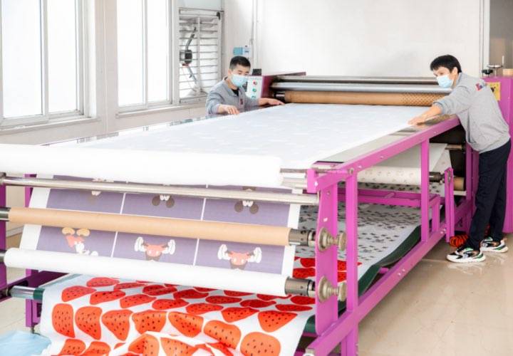 Two workers are operating a digital printing machine to print on fabric.