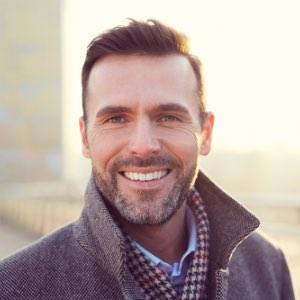 A man wearing a dark gray coat smiles at the camera.